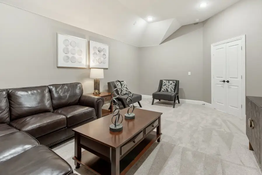 Finished basement living area with dark leather sofa, gray accent chairs, wood coffee table, and neutral carpet