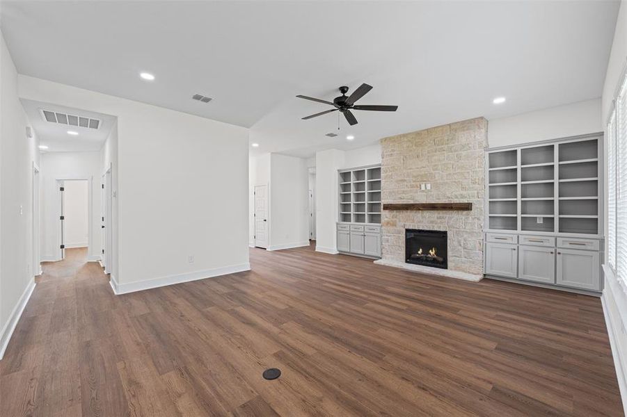 Living area featuring rich wood flooring, a stone fireplace with a wooden mantel, and built-in shelving with cabinetry