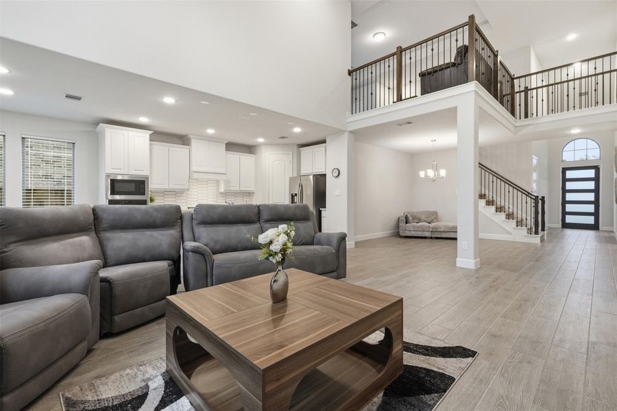 This spacious living area features an open floor plan with high ceilings. The kitchen boasts white cabinetry and stainless steel appliances. A staircase leads to a loft area, and abundant natural light enhances the welcoming atmosphere. This spacious living area features an open floor plan with high ceilings. The kitchen boasts white cabinetry and stainless steel appliances. A staircase leads to a loft area, and abundant natural light enhances the welcoming atmosphere.