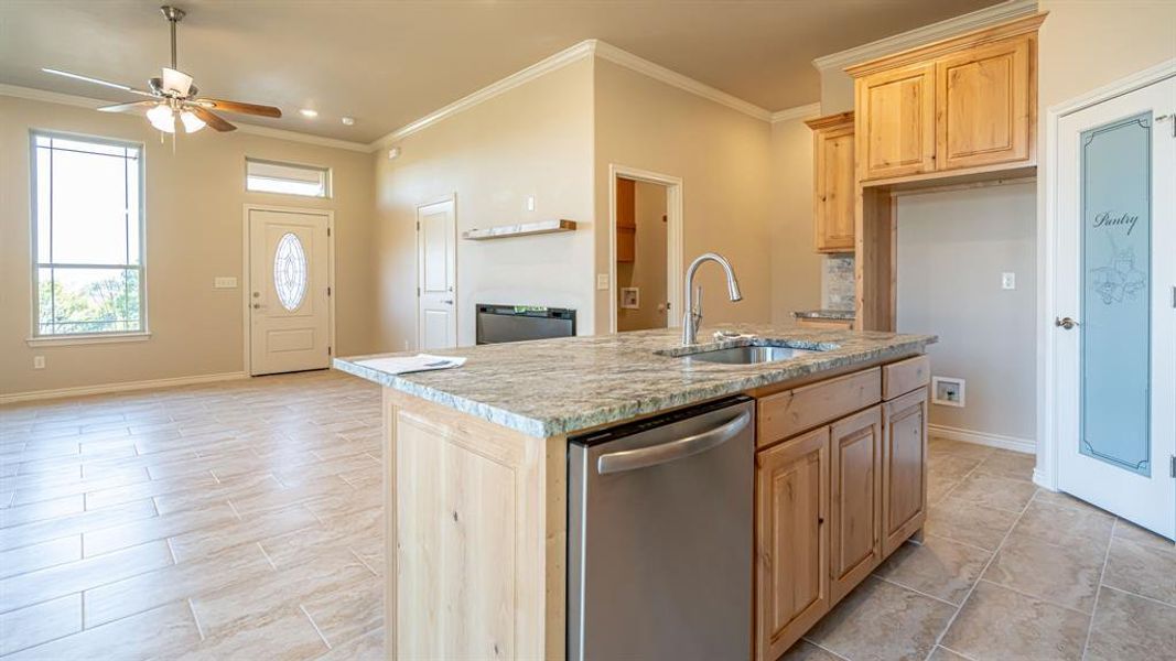 Kitchen featuring stainless steel dishwasher, crown molding, open floor plan, light brown cabinetry, and light stone countertops