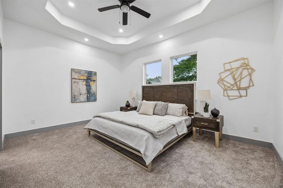 Spacious primary bedroom featuring a tray ceiling with recessed lighting and a ceiling fan