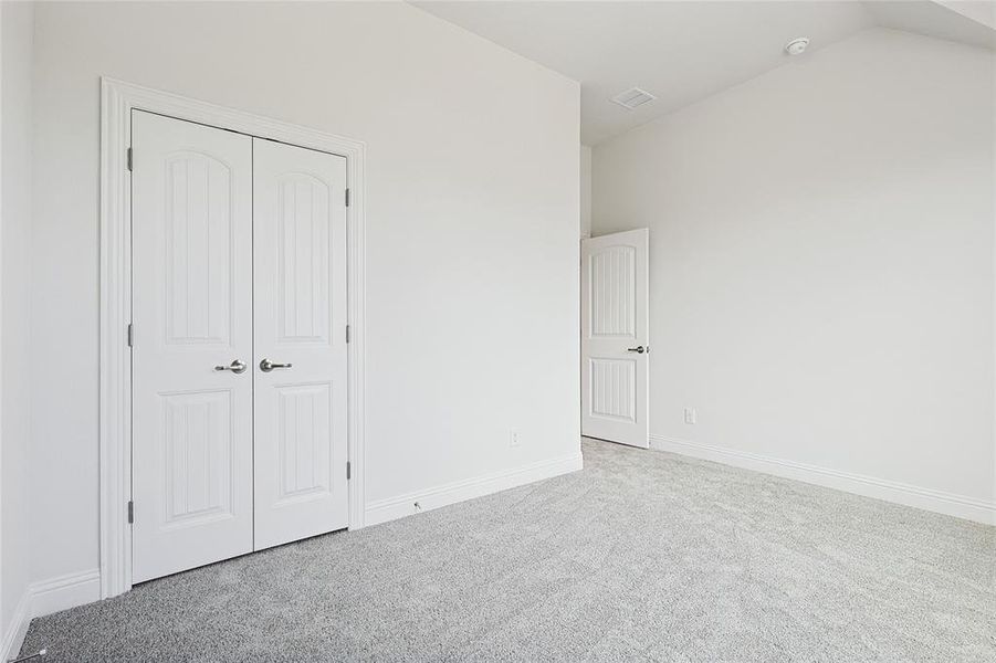 Unfurnished bedroom with light colored carpet, a closet, and lofted ceiling