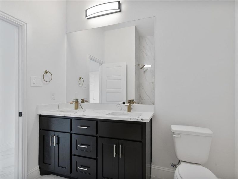 Full bath featuring double vanity, toilet, baseboards, and a marble finish shower