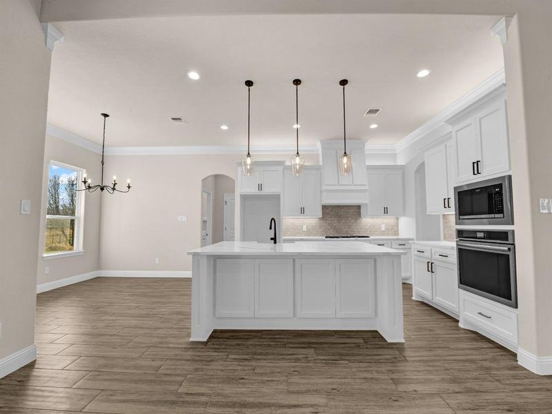 Kitchen featuring white cabinets, oven, a kitchen island with sink, and built in microwave