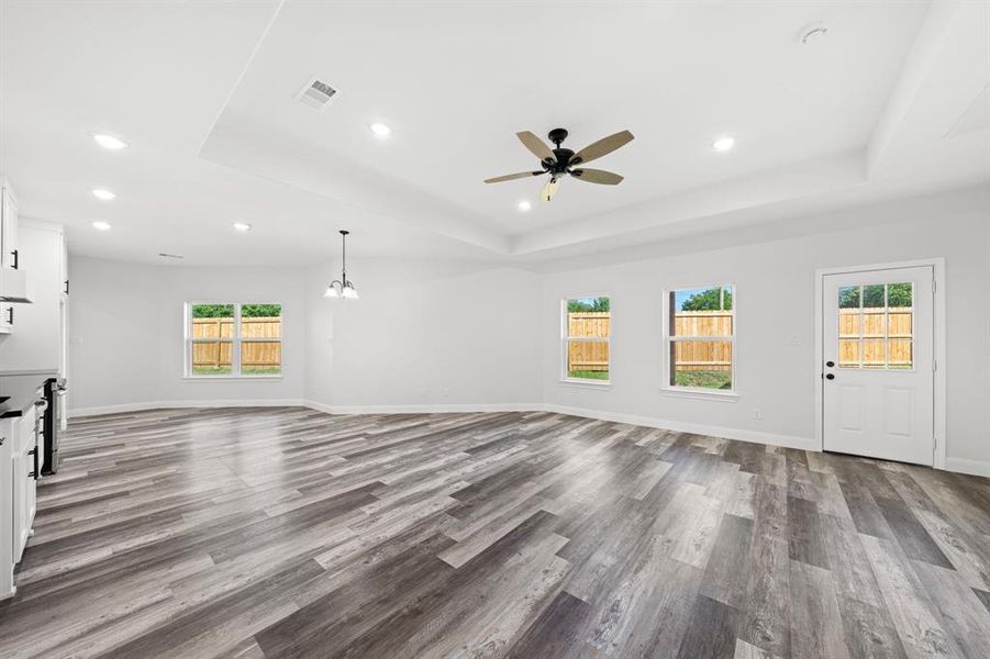 Unfurnished living room with a raised ceiling, dark wood finished floors, a ceiling fan, recessed lighting, and a chandelier Unfurnished living room with a raised ceiling, dark wood finished floors, a ceiling fan, recessed lighting, and a chandelier