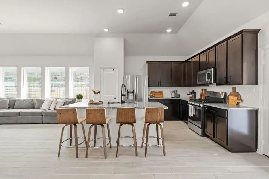 The kitchen boasts a spacious island with a sleek black faucet and sink. Finished with stainless steel appliances, a 5 burner gas cooktop, and sleek wood cabinets, this kitchen is ideal for cooking for the whole family or hosting holidays!