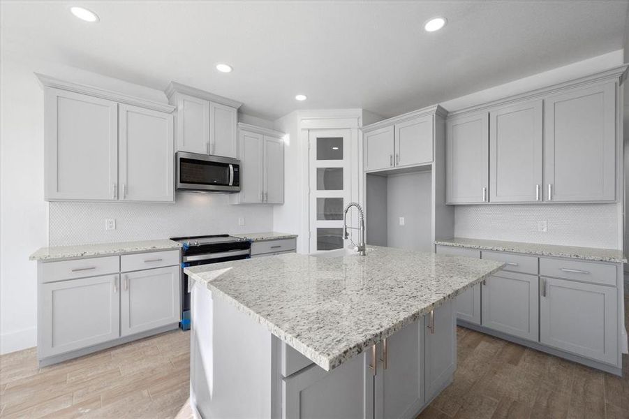 Kitchen featuring sink, light stone countertops, a center island with sink, appliances with stainless steel finishes, and light hardwood / wood-style flooring