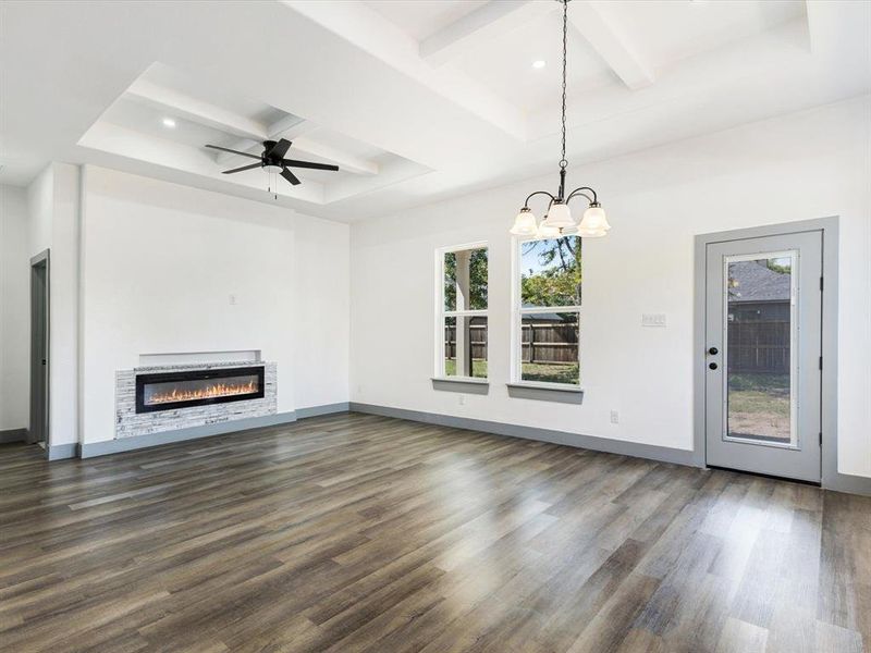Unfurnished living room with beamed ceiling, coffered ceiling, dark wood finished floors, a glass covered fireplace, and a ceiling fan Unfurnished living room with beamed ceiling, coffered ceiling, dark wood finished floors, a glass covered fireplace, and a ceiling fan