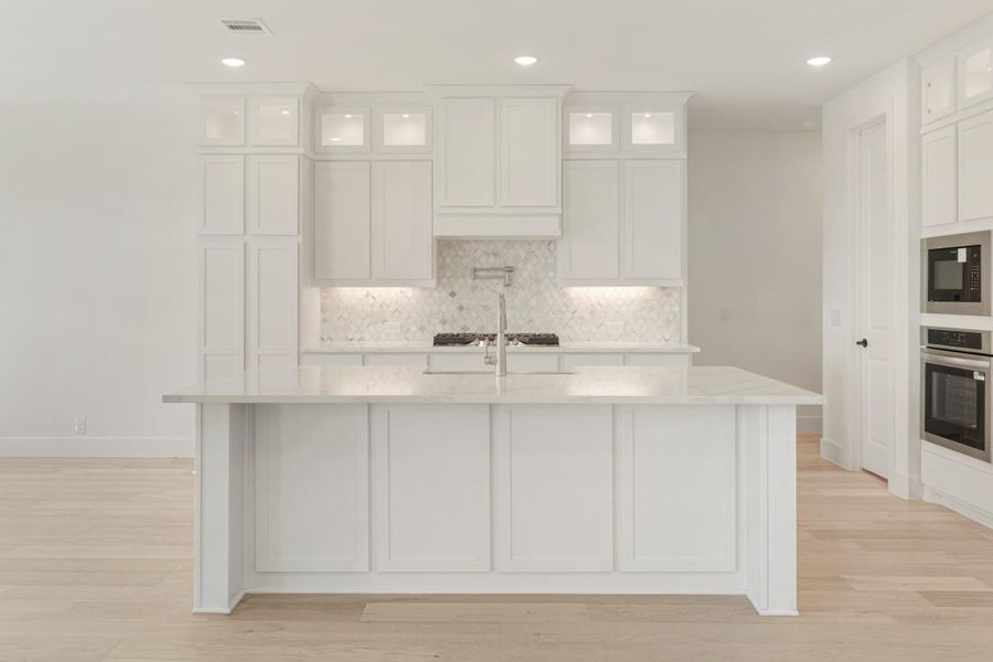 White kitchen with large island, marble countertops, herringbone tile backsplash, and light hardwood floors