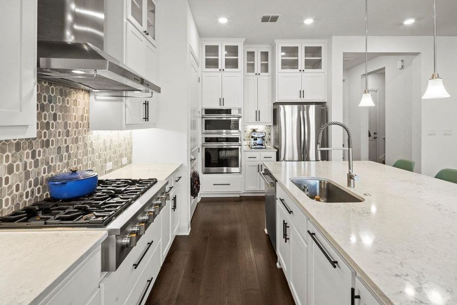 Kitchen with visible vents, light stone counters, stainless steel appliances, wall chimney exhaust hood, and a sink