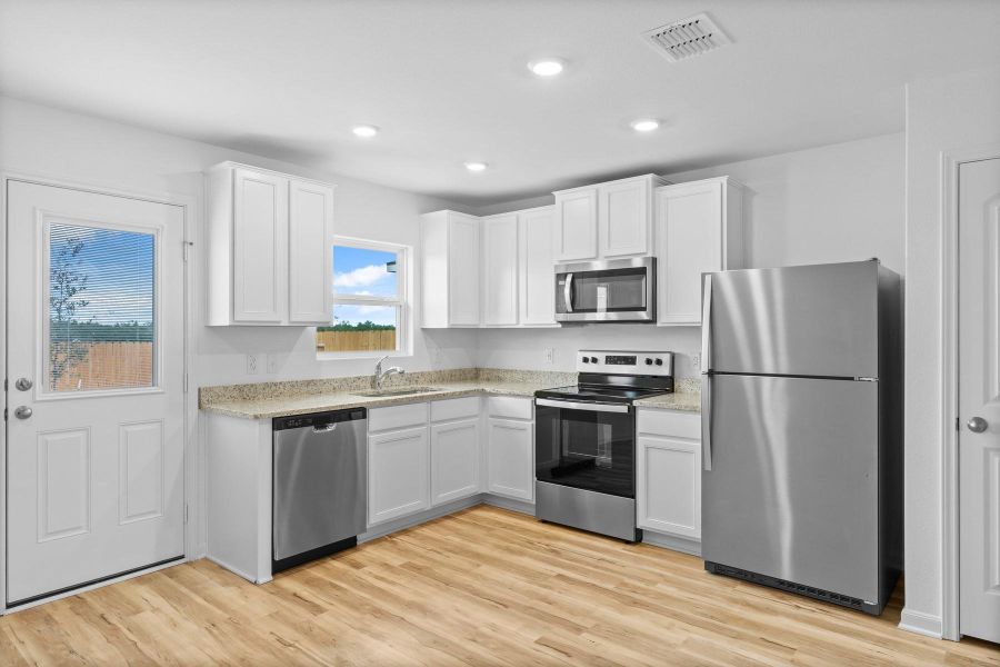 Kitchen with appliances with stainless steel finishes, light wood-style floors, white cabinetry, light stone counters, and recessed lighting