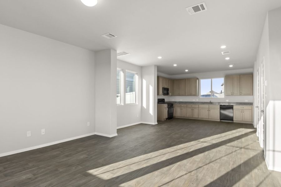 Image of living and dining room area with dark brown wood-like flooring and light grey painted walls with a kitchen in the distance