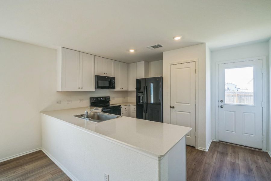 A well-equipped kitchen features modern black appliances and a convenient peninsula with a sink, all beneath recessed lighting. A well-equipped kitchen features modern black appliances and a convenient peninsula with a sink, all beneath recessed lighting.