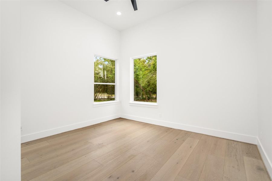 One of two first-floor secondary bedrooms (13x11), each showcasing stunning white oak floors, ample closet space, remote-controlled ceiling fans, and abundant natural light One of two first-floor secondary bedrooms (13x11), each showcasing stunning white oak floors, ample closet space, remote-controlled ceiling fans, and abundant natural light