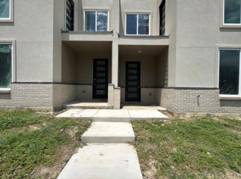 Property entrance with brick siding, stucco siding, and a lawn Property entrance with brick siding, stucco siding, and a lawn