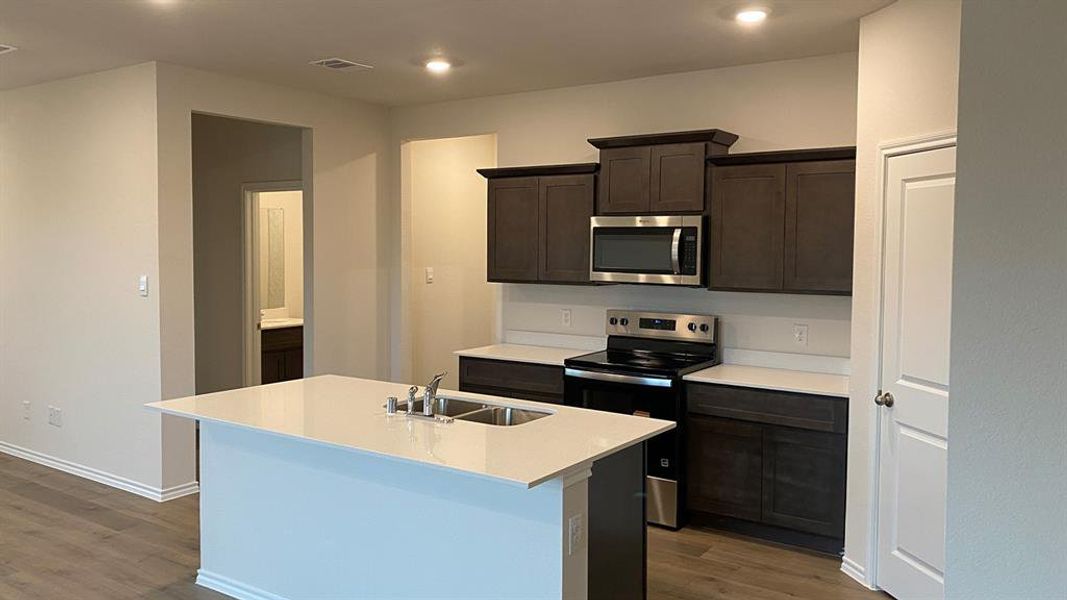 Kitchen featuring stainless steel appliances, dark wood finish cabinets, a center island with sink, dark wood finished floors, and recessed lighting