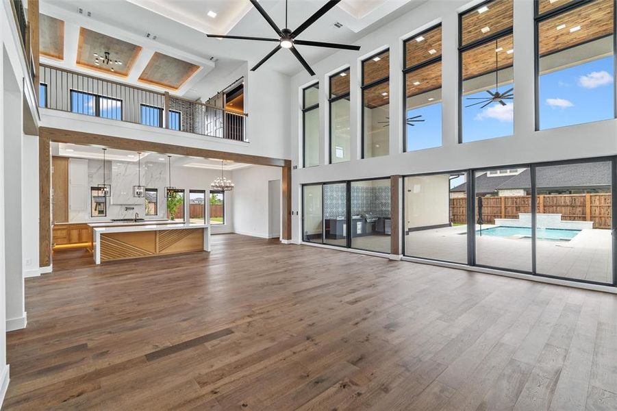 Unfurnished living room featuring wood-type flooring, a towering ceiling, coffered ceiling, and ceiling fan with notable chandelier