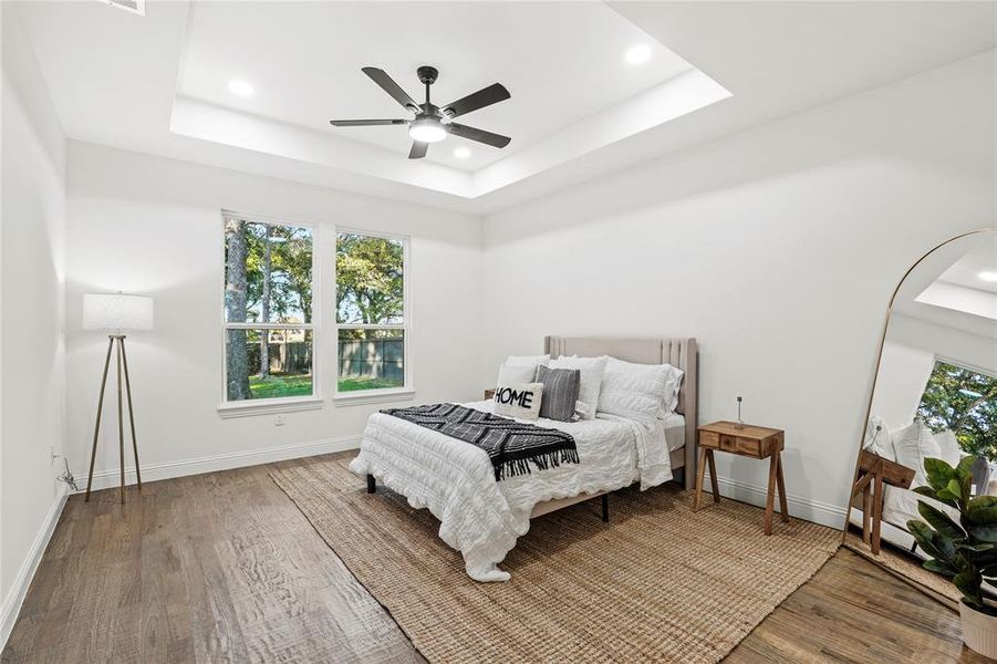 Bedroom featuring multiple windows, wood finished floors, a tray ceiling, and recessed lighting