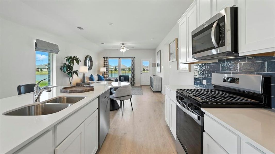 Kitchen with stainless steel appliances, white cabinets, tasteful backsplash, light wood-style floors, and open floor plan