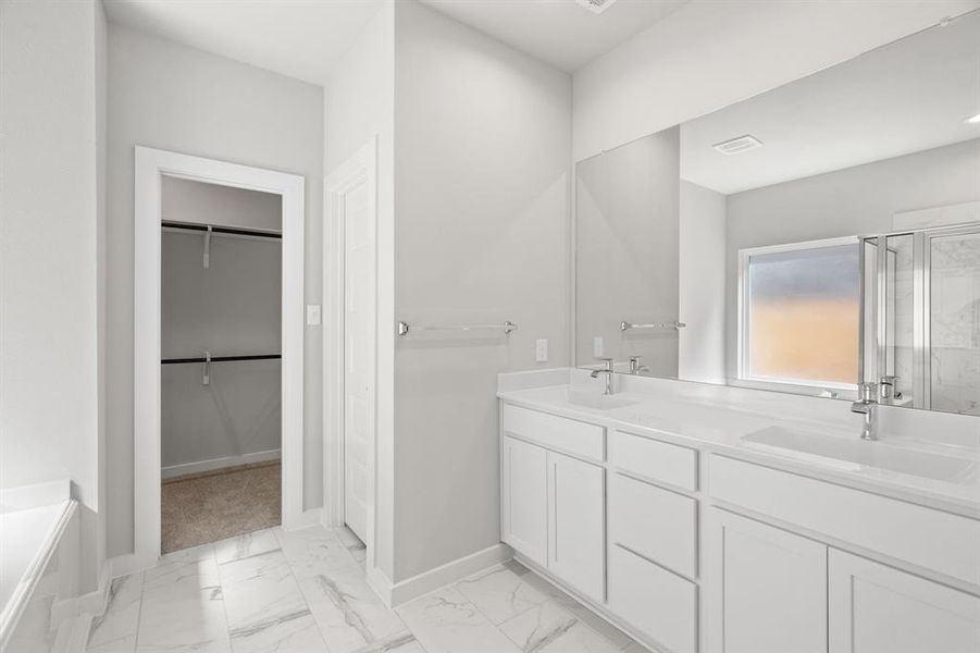 Escape to a spa-like oasis in this primary bathroom. Enjoy a walk-in shower with tile surround, a separate garden tub with custom detailing, and an elegant vanity featuring light countertops, modern hardware, and bright recessed lights. Sample photo of completed home with similar floor plan. As-built interior colors and selections may vary.