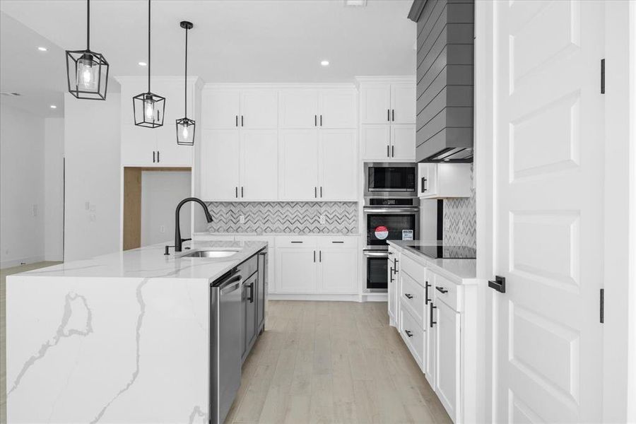 Spacious kitchen featuring a large island with a waterfall-edge countertop, an undermount sink, and integrated dishwasher