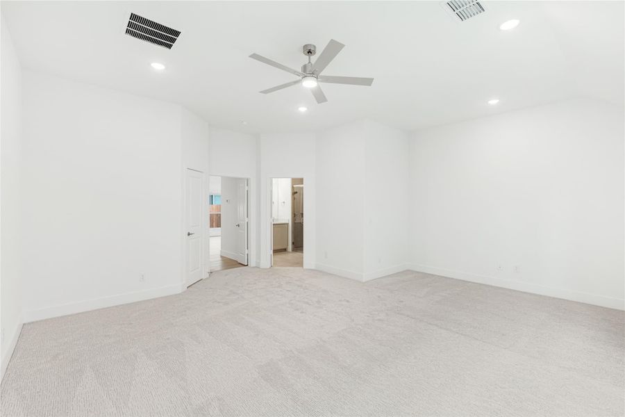Spacious empty bedroom with light carpet, ceiling fan, and open doorway to ensuite bathroom