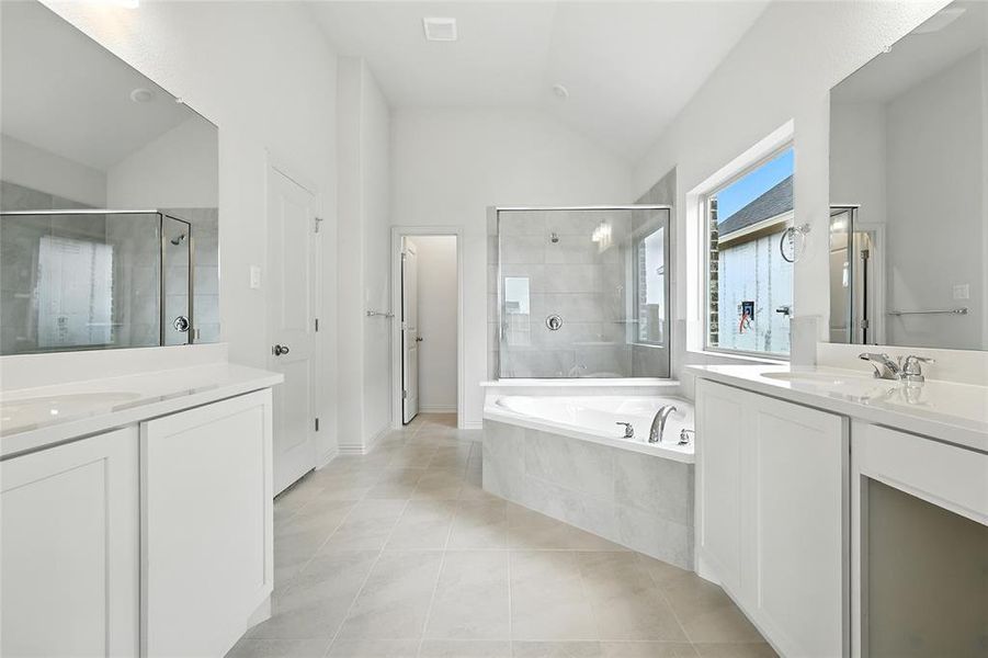Bathroom with a stall shower, a bath, two vanities, light tile patterned floors, and vaulted ceiling