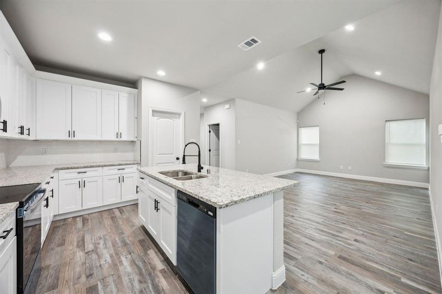 Kitchen with backsplash, granite countertops, white cabinetry, lofted ceiling, light wood finished floors, and stainless steel appliances Kitchen with backsplash, granite countertops, white cabinetry, lofted ceiling, light wood finished floors, and stainless steel appliances
