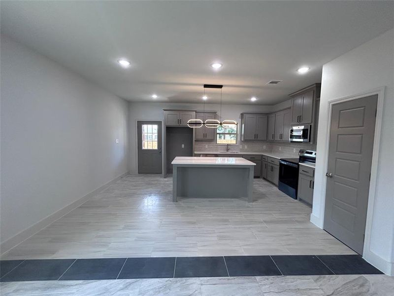 Kitchen with stainless steel appliances, a center island, light countertops, backsplash, and gray cabinets Kitchen with stainless steel appliances, a center island, light countertops, backsplash, and gray cabinets