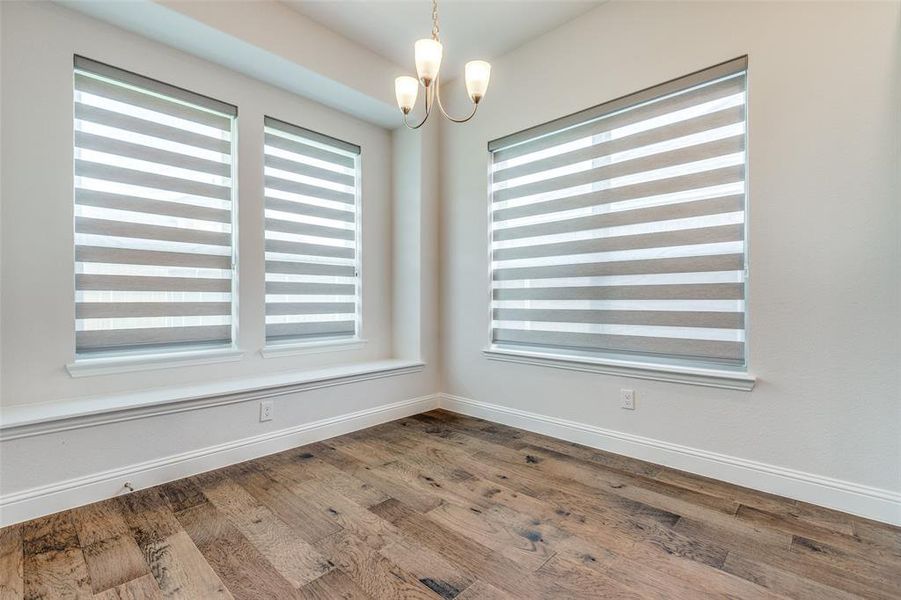 Spare room with a chandelier, healthy amount of natural light, wood finished floors, and baseboards