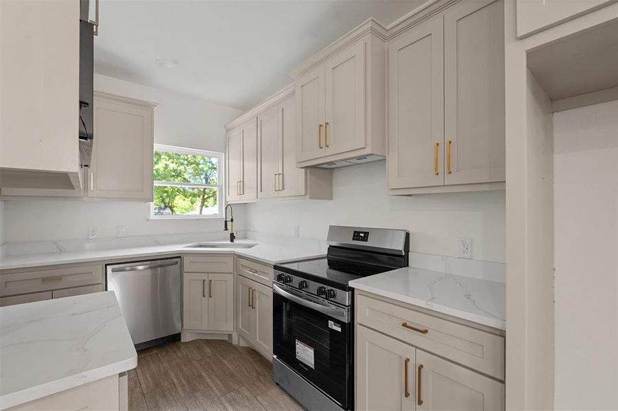 Contemporary kitchen featuring light wood-finish cabinetry, white countertops, stainless steel appliances, a corner sink with a gooseneck faucet, and wood-look flooring
