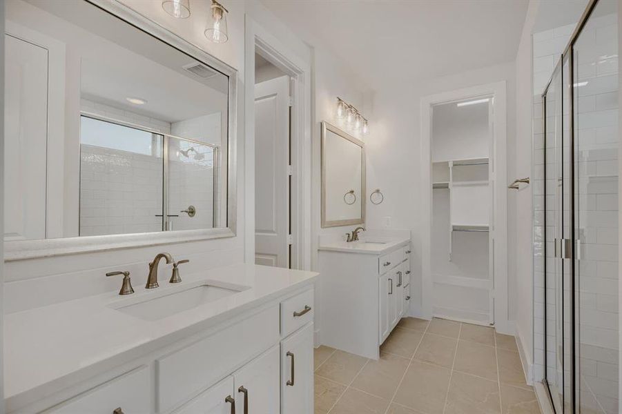 Dual vanity bathroom featuring white cabinetry, bronze fixtures, a glass-enclosed shower, and built-in closet shelving