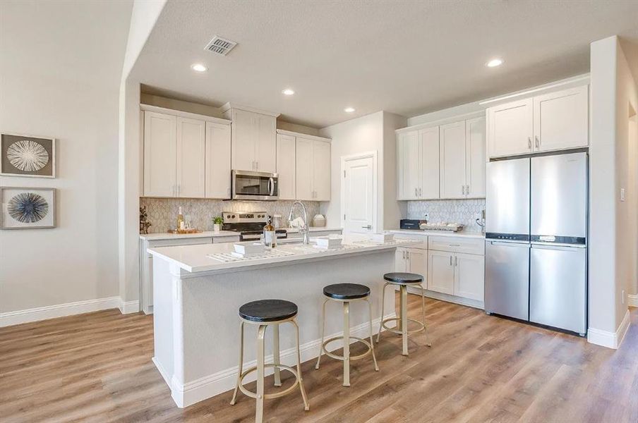 Kitchen with white cabinets, a kitchen bar, a kitchen island with sink, stainless steel appliances, and light wood-type flooring