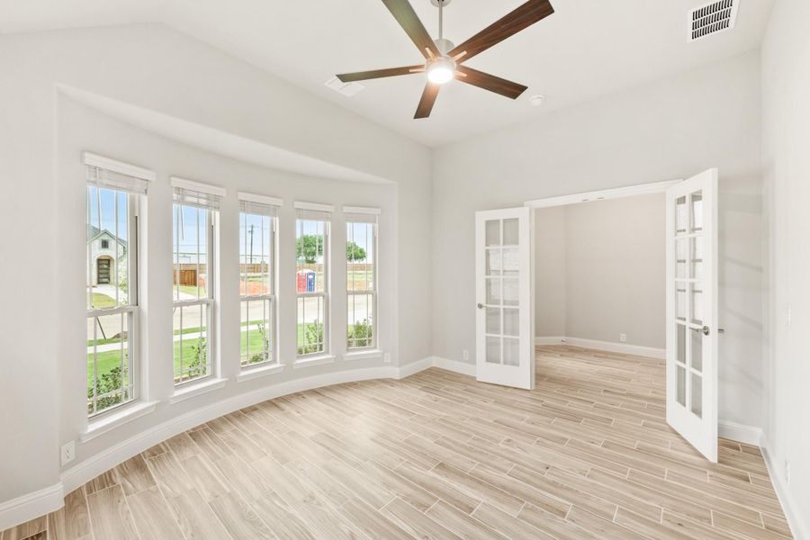 Empty room with light wood-look tile floors, ceiling fan, large windows, and French doors Empty room with light wood-look tile floors, ceiling fan, large windows, and French doors