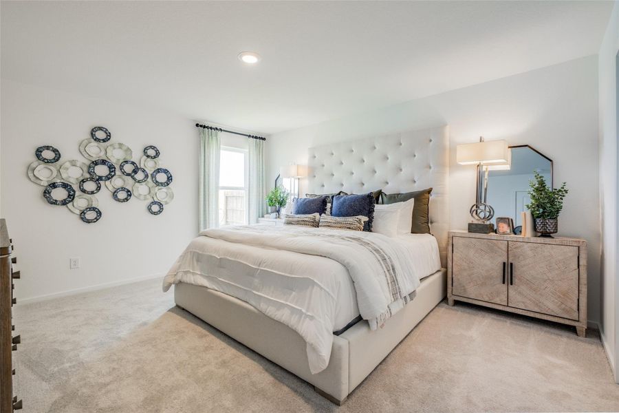 This bedroom features a plush, upholstered bed with elegant bedding, a stylish wall art installation, and a modern dresser. Soft carpeting and ample natural light create a cozy, inviting atmosphere.