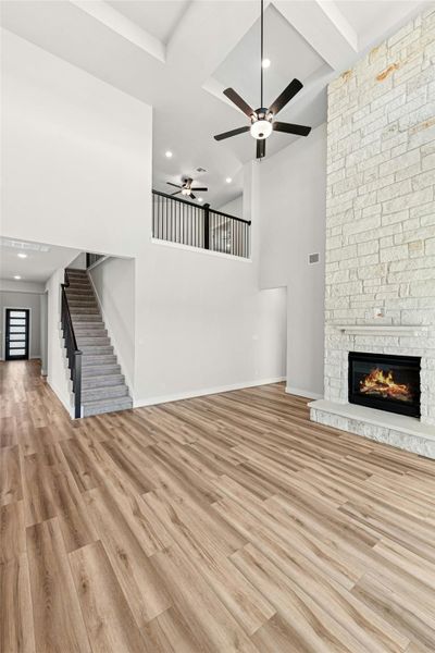 Unfurnished living room featuring light wood-type flooring, stairway, coffered ceiling, a fireplace, and a high ceiling