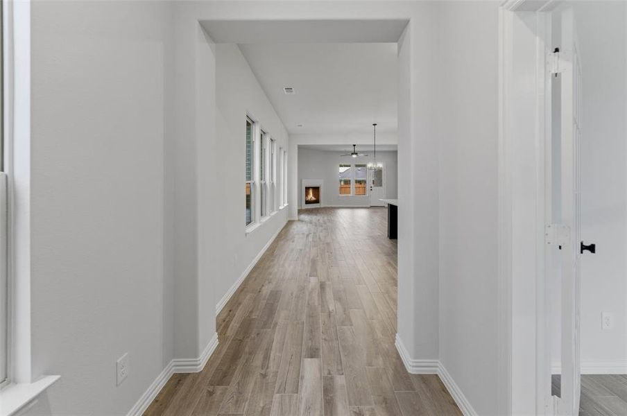 Spacious interior hallway featuring wood-finish flooring, white baseboards, and a series of windows providing natural light