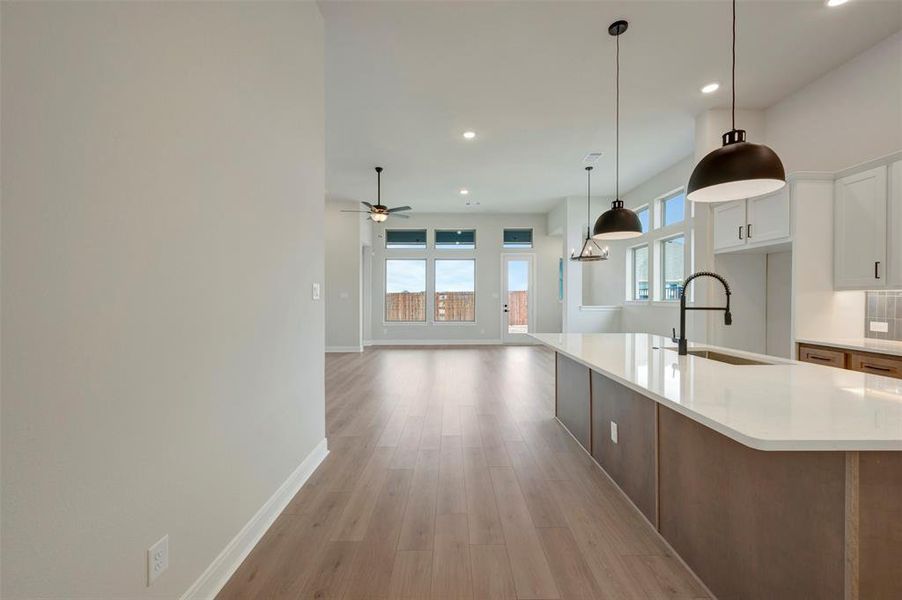Kitchen featuring light wood finished floors, decorative light fixtures, light stone countertops, white cabinets, and open floor plan