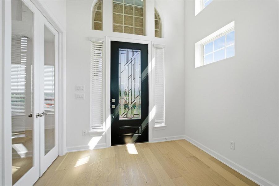 Two-story entry featuring light wood-finish flooring, a dark entry door with decorative glass, an arched transom window with glass block, and French doors with clear glass panels