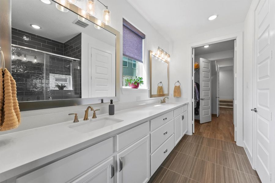 The luxurious primary bathroom features a double vanity with quartz countertops and modern finishes. This space is designed to feel like a spa-like retreat within the home.