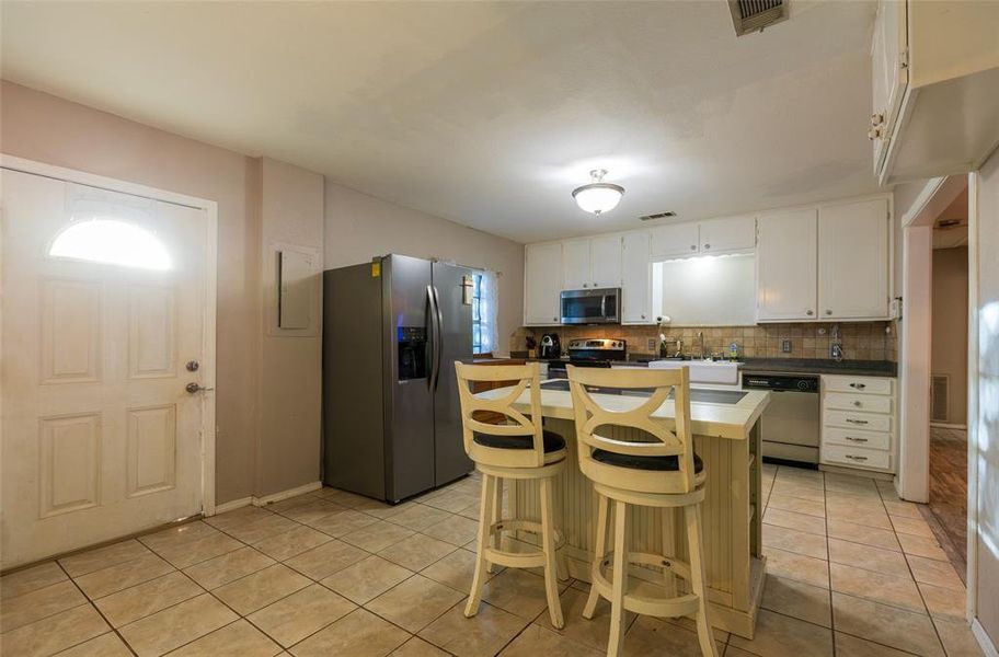 Kitchen with stainless steel appliances, a kitchen island, light tile patterned flooring, tasteful backsplash, and a kitchen bar Kitchen with stainless steel appliances, a kitchen island, light tile patterned flooring, tasteful backsplash, and a kitchen bar