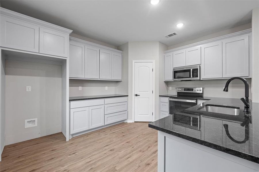 Kitchen with light wood-style flooring, dark stone counters, appliances with stainless steel finishes, white cabinets, and recessed lighting