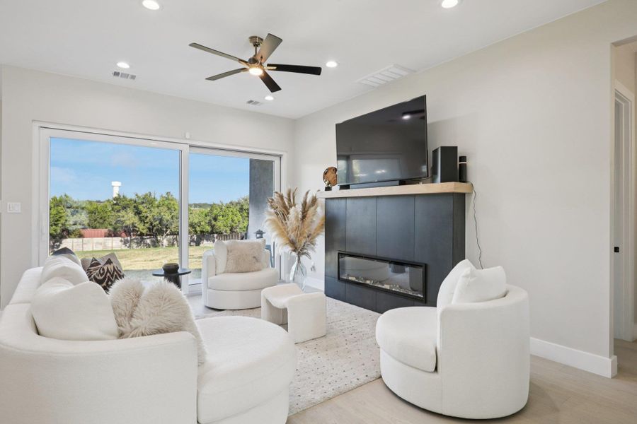 Living room featuring a glass covered fireplace, wood finished floors, a ceiling fan, and recessed lighting