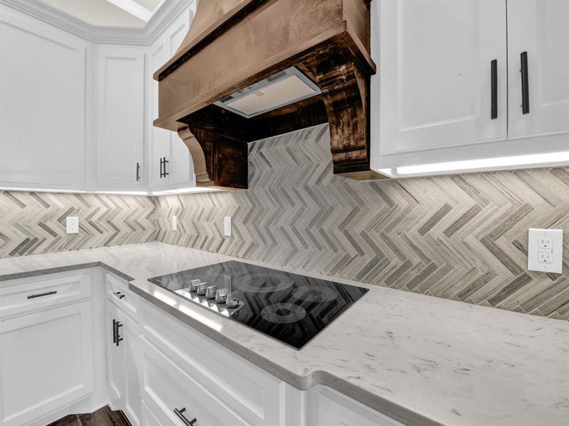 Kitchen featuring custom range hood, white cabinetry, light stone counters, backsplash, and black electric stovetop Kitchen featuring custom range hood, white cabinetry, light stone counters, backsplash, and black electric stovetop
