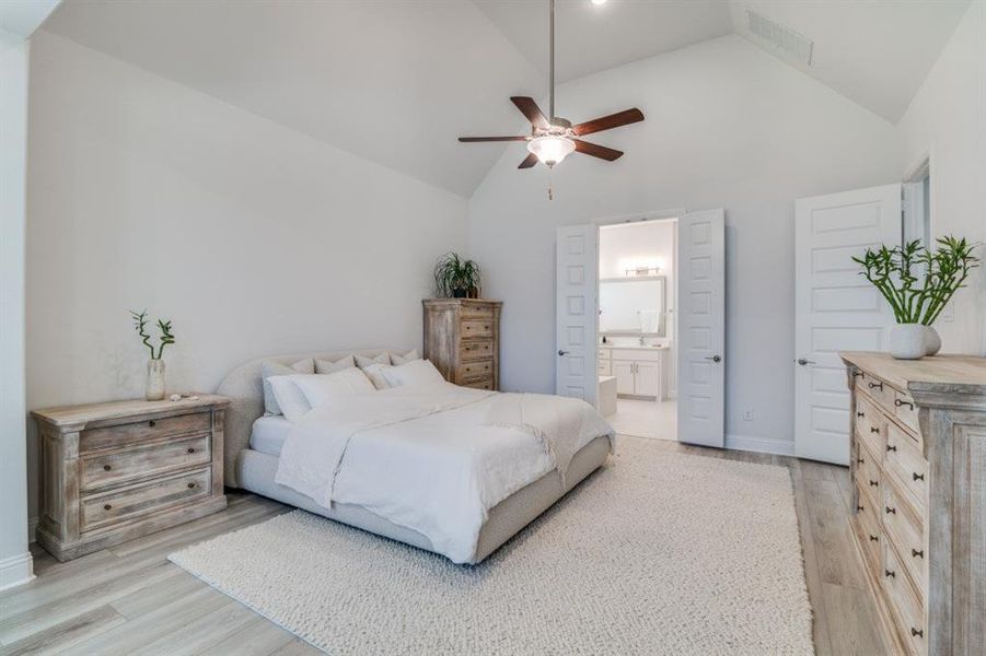 Bedroom with high vaulted ceiling, a ceiling fan, light wood-style flooring, ensuite bath, and visible vents Bedroom with high vaulted ceiling, a ceiling fan, light wood-style flooring, ensuite bath, and visible vents
