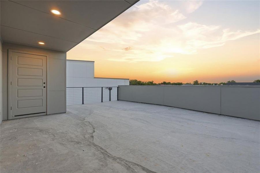 Expansive rooftop terrace featuring a concrete surface, contemporary panel door, recessed lighting, and perimeter wall