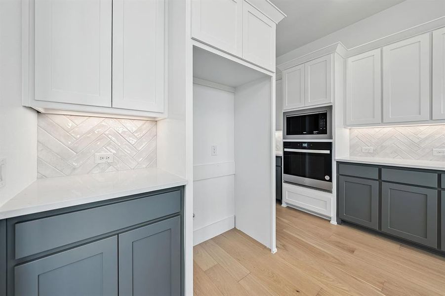Kitchen featuring tasteful backsplash, gray cabinetry, white cabinetry, and stainless steel oven
