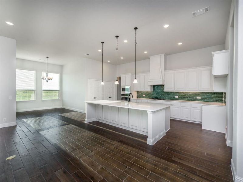 Kitchen featuring white cabinetry, an island with sink, backsplash, recessed lighting, and decorative light fixtures