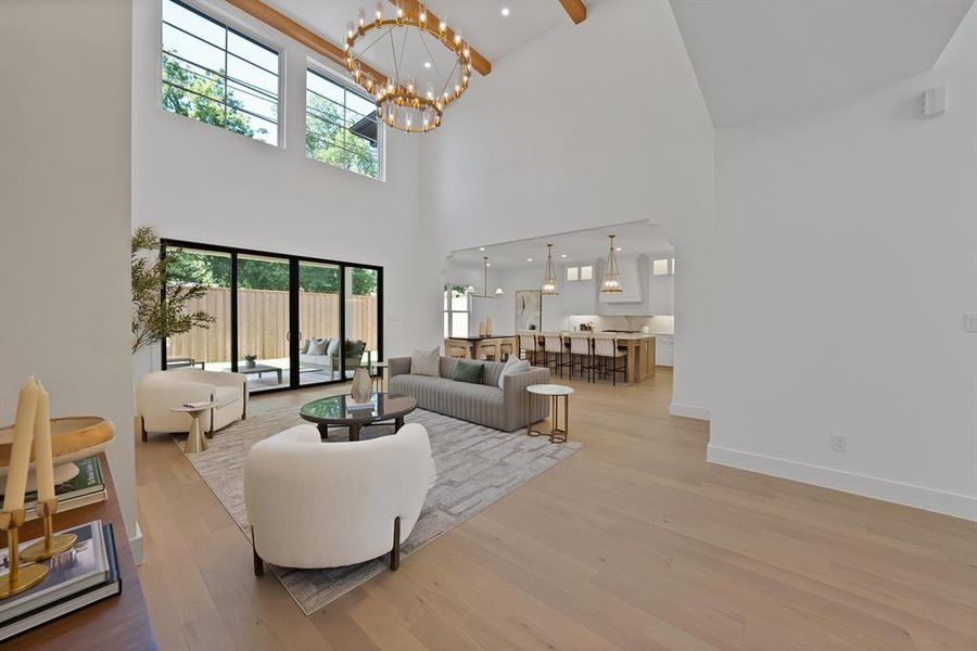 Vaulted ceiling great room with wood-finish flooring, featuring a large chandelier, upper transom windows, and expansive sliding glass doors