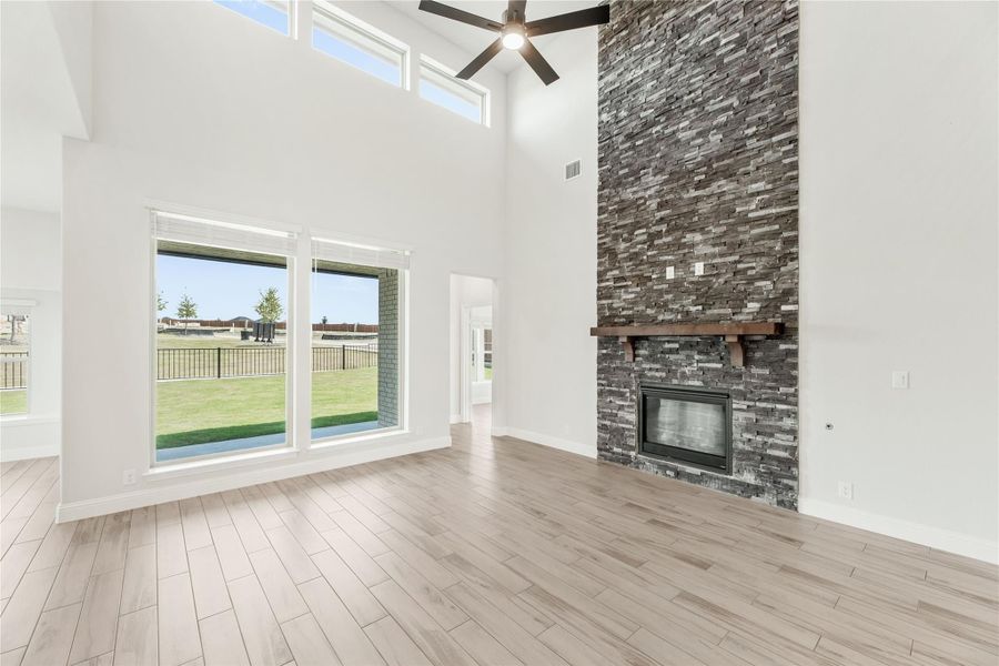 Open living room with two-story ceiling, stacked stone fireplace, ceiling fan, and light wood floors